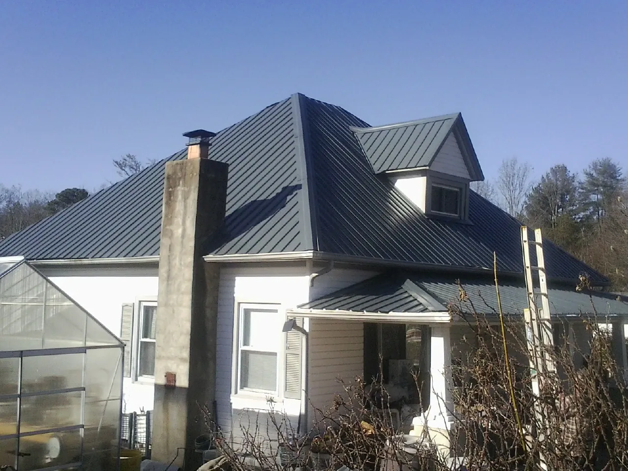 Dark blue standing seam metal roof on a white farmhouse with dormer — Slate & Tile Roof Repair by Roofing Brothers in Boomer
