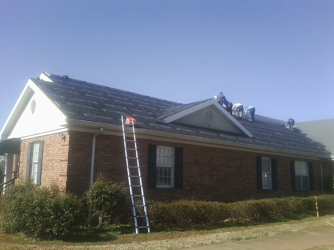 Crew tearing shingles off a brick ranch roof with a ladder set — Emergency Roof Repair work by our crew in Boomer