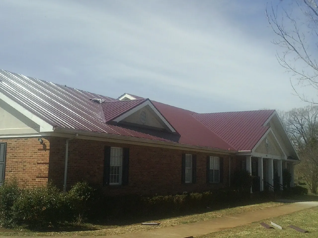 Red metal roof with gabled entries on a long brick building, from a Hail Damage Roof Repair job in Boomer