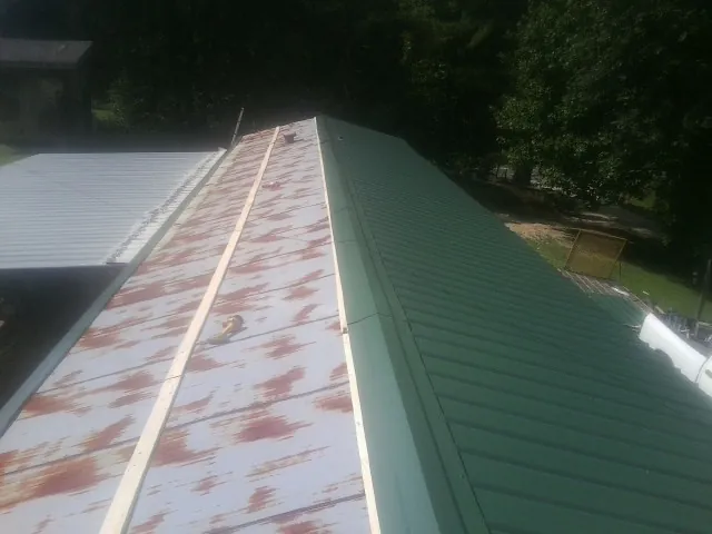 Old rusted panels beside newly installed green metal roofing — Wind Damage Roof Repair by Roofing Brothers in Boomer