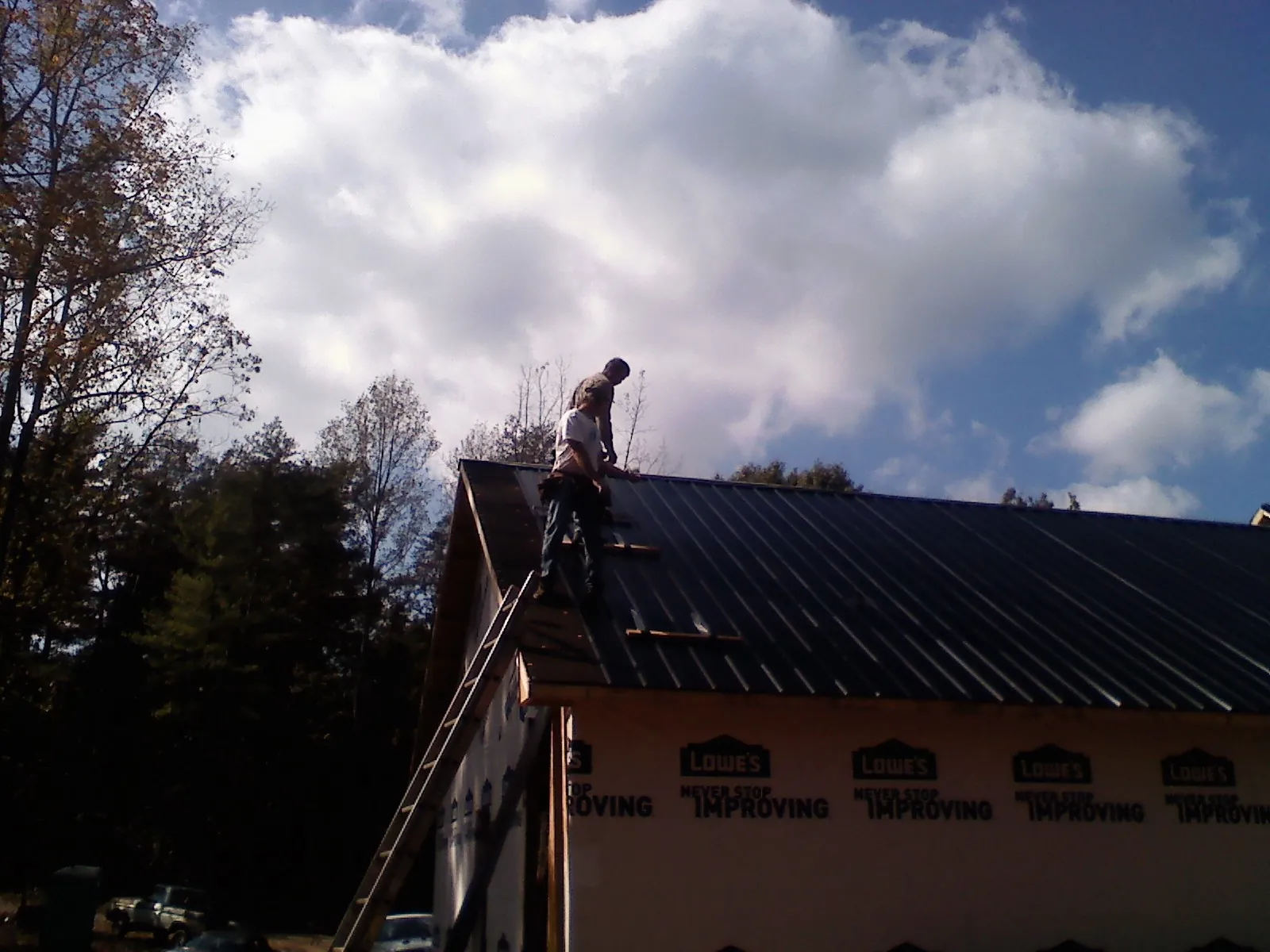 Roofer fastening dark metal panels high against a cloudy sky, from a Roof Inspection job in Boomer