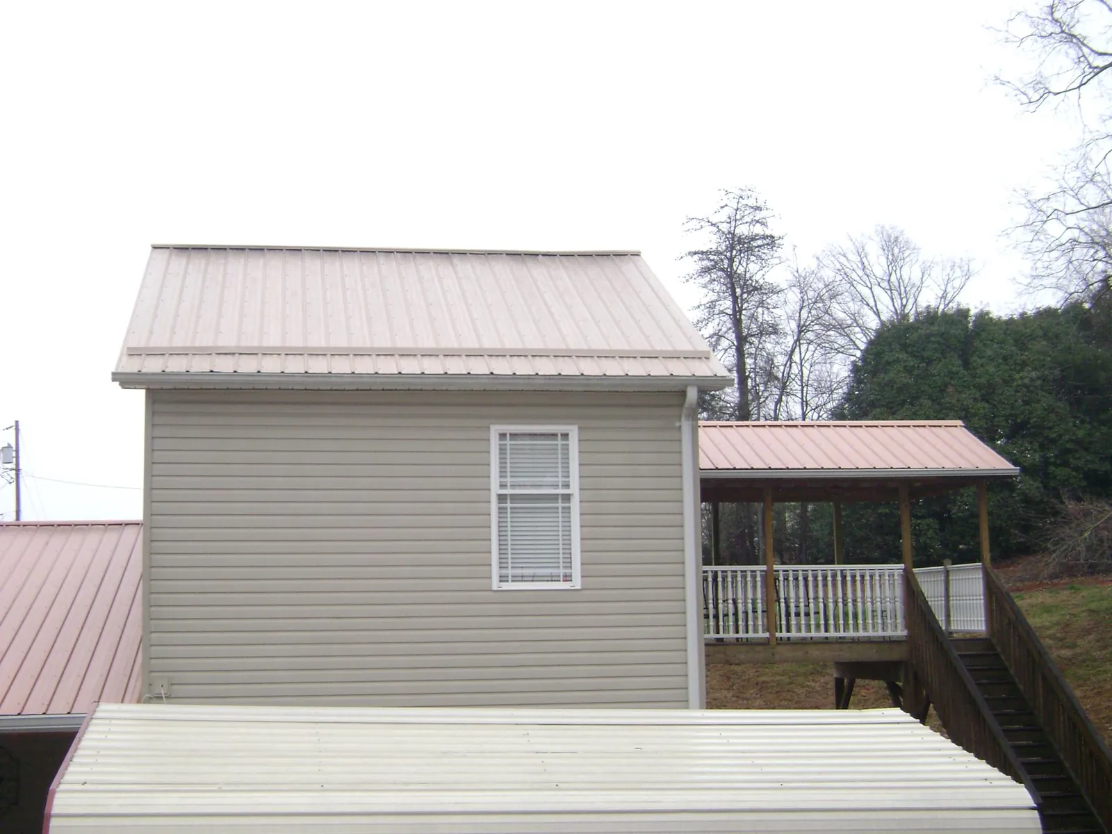Tan metal roofs on a two story addition and attached porch, from a Roof Replacement job in Boomer